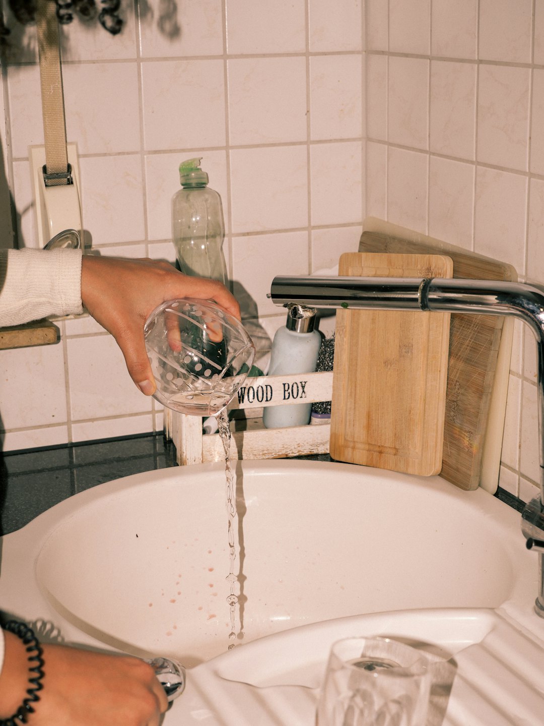 Ręce przelewają wodę z wzorzystego szklanego dzbanka do zlewu.